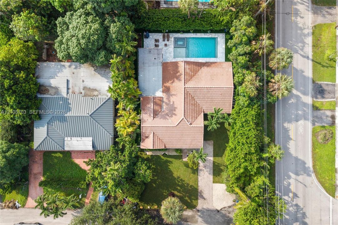 Aerial perspective featuring a tile-roof residence, a rectangular swimming pool, integrated spa, paved patio area, and mature landscaping