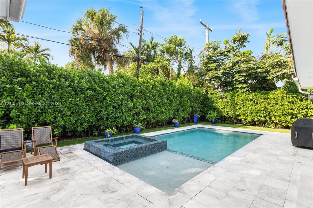 Backyard featuring a swimming pool with a built-in spa, stone patio, and perimeter privacy hedges