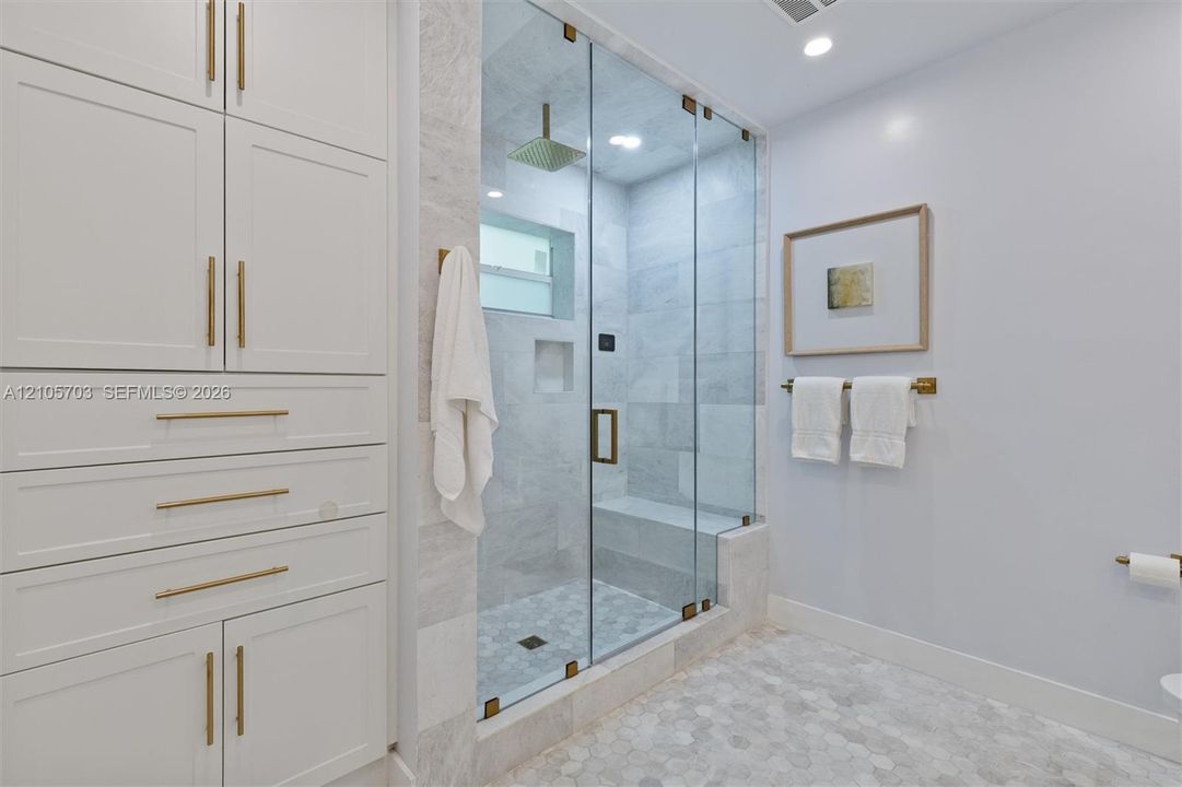 Walk-in steam shower featuring a glass enclosure, built-in stone bench, and rainfall showerhead, accompanied by custom floor-to-ceiling cabinetry with brass-finish hardware