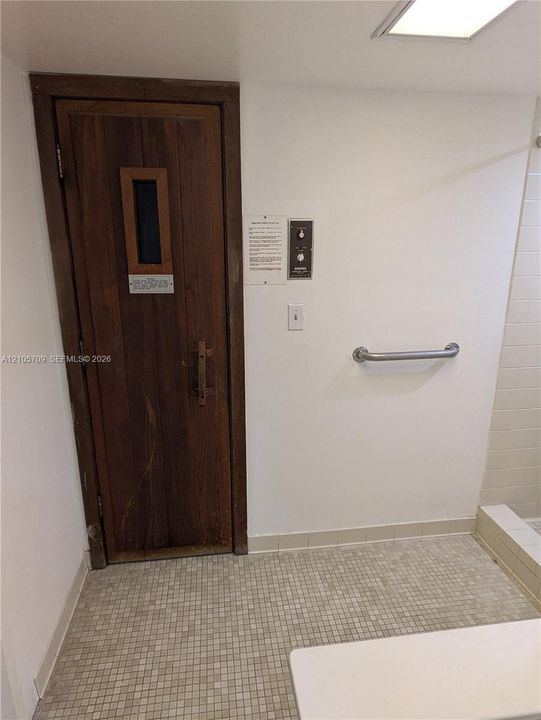 Sauna featuring a wood door with a vertical glass insert, wall-mounted control panel, and tiled flooring
