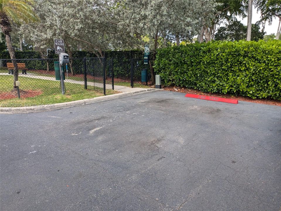 Paved parking area featuring a dedicated car wash station, chain-link perimeter fencing, and mature hedge landscaping