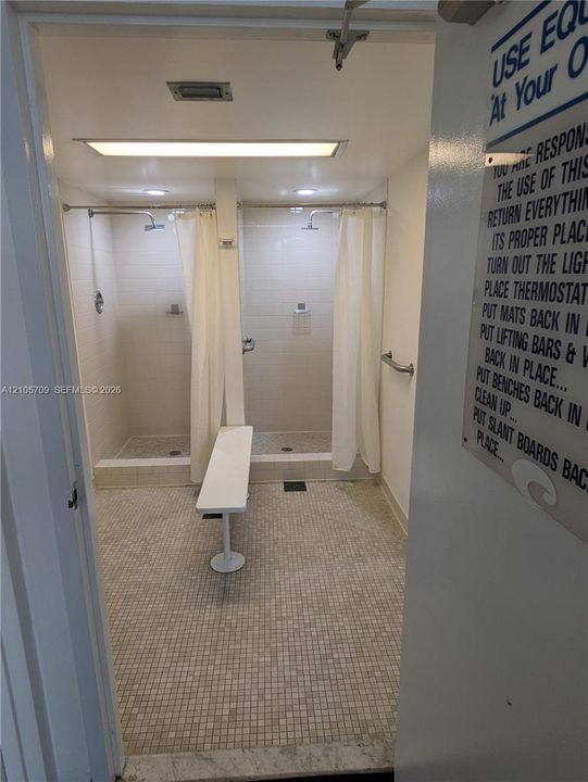 Dual shower stalls featuring tile surround, mosaic floor tiling, wall-mounted metal grab bars, and recessed lighting