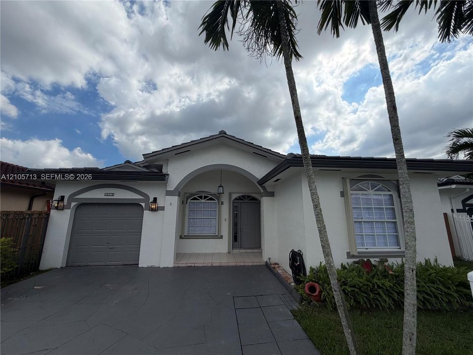 Single-story stucco exterior featuring a tiled roof, arched entryway, arched window accents, and a paved driveway