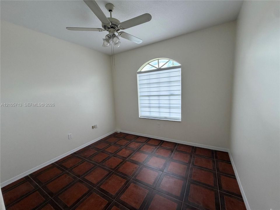 Room featuring terra cotta-style tile flooring, an arched window with integrated mullions, and a central ceiling fan with multi-light fixture