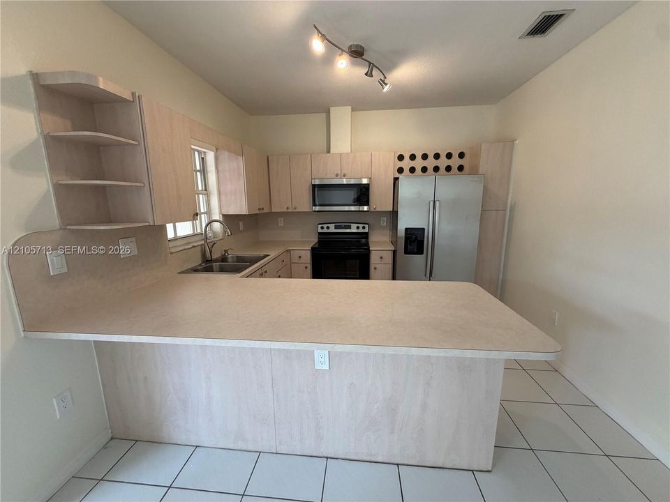 Kitchen featuring light-tone cabinetry, built-in wine storage, solid surface countertops, stainless steel appliances, and ceramic tile flooring