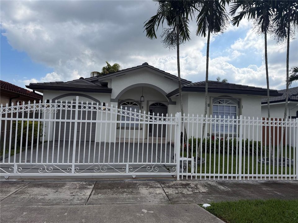 Single-story residence featuring a gated entry, arched front porch, tile roof, arched windows, and mature palm trees