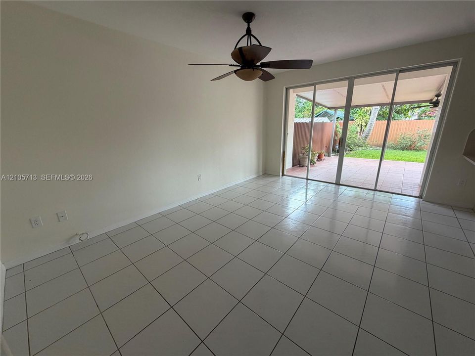 Interior space featuring neutral wall paint, white tile flooring, a ceiling fan with integrated lighting, and full-height sliding glass doors opening to a covered patio and enclosed lawn
