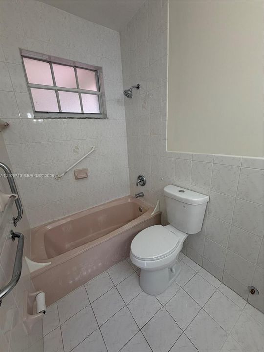 Bathroom featuring full-height wall tiling, white ceramic tile flooring, a built-in tub, and a multi-pane window