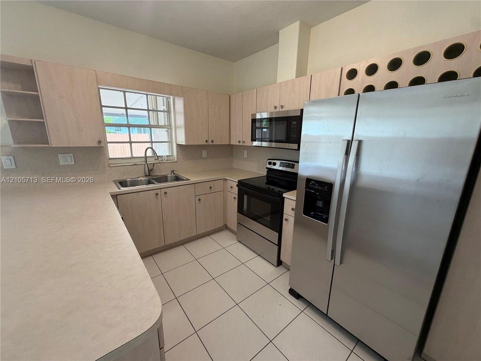 Kitchen featuring light-finish cabinetry, built-in wine rack storage, stainless steel appliances, double-basin sink, and tile flooring