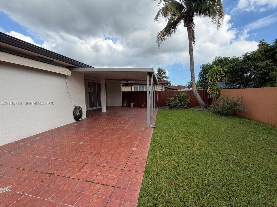 Covered patio with tile flooring and a ceiling fan, featuring an enclosed backyard with a lawn and perimeter fencing