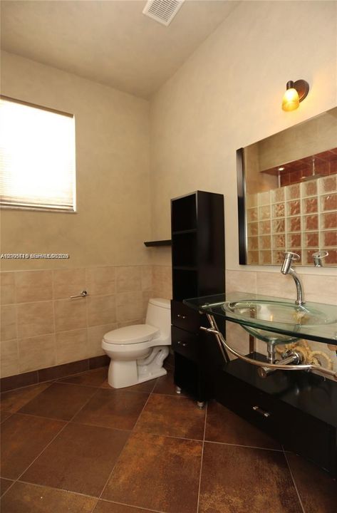 Bathroom featuring a glass vessel sink, dark cabinetry, ceramic tile flooring, and a glass block accent wall