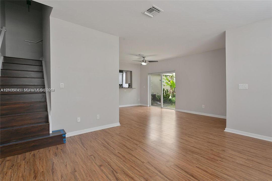 Open interior featuring wood-finish flooring, a staircase with dark wood-finish treads, a neutral wall palette, a ceiling-mounted fan, and glass sliding doors