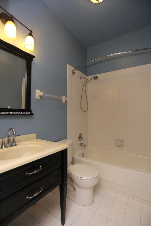 Bathroom featuring a black vanity with a molded countertop, a curved shower rod, a handheld showerhead, and a ceramic tile floor