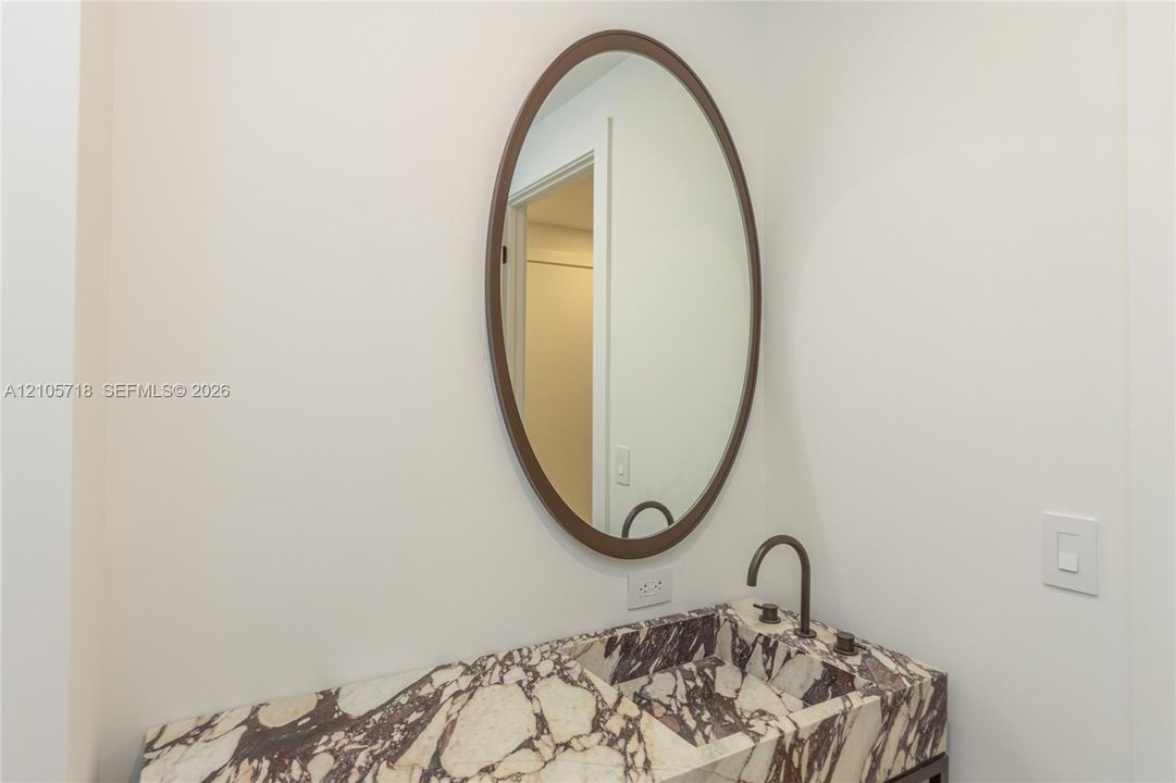 Stone countertop with an integrated basin, oval wall-mounted mirror with a bronze-toned frame, and a bronze-toned gooseneck faucet