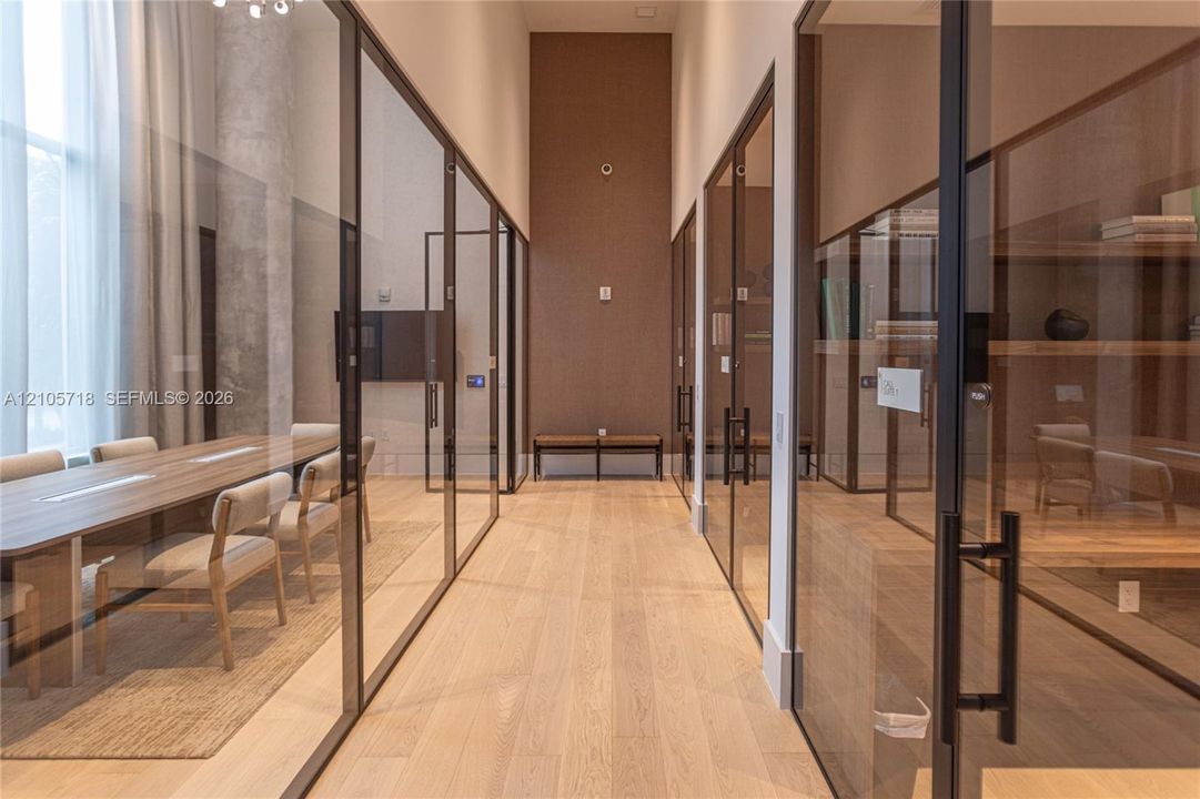 Hallway featuring full-height glass partitions with matte black framing, wood-finish flooring, high ceilings, and built-in shelving