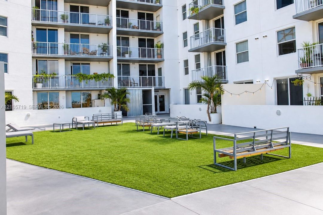Outdoor courtyard featuring a manicured lawn, smooth concrete perimeter, perimeter wall lighting, and established palm trees