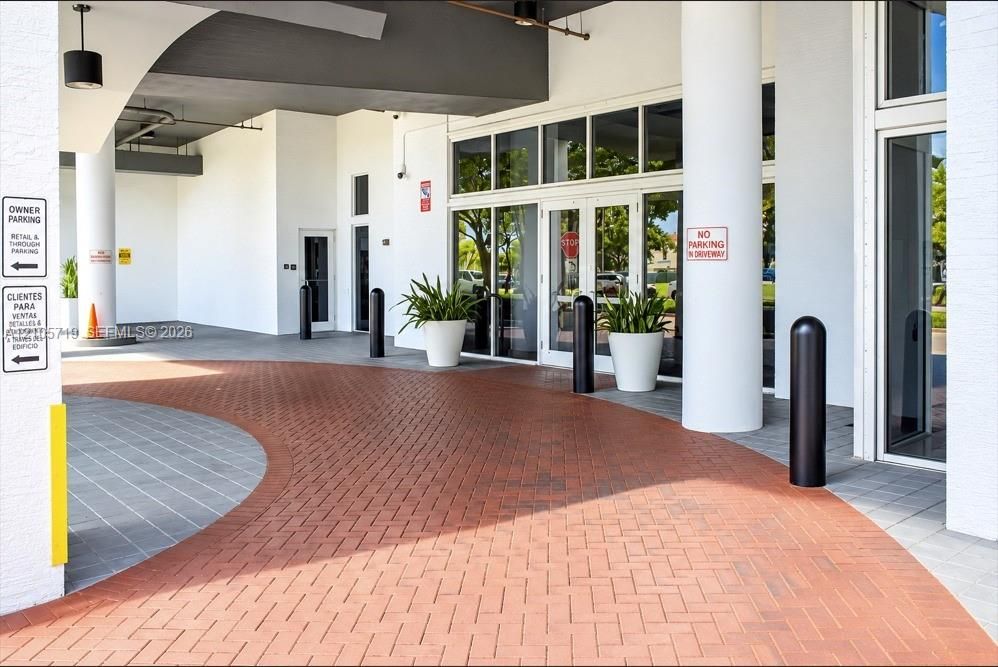 Covered porte-cochère entrance featuring herringbone-patterned brick paving, structural pillars, and a glass-paneled double-door entryway