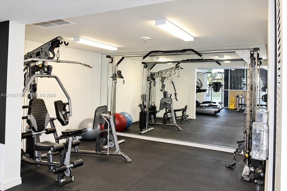 Fitness center featuring wall-to-wall mirrors, durable rubberized flooring, and dual overhead linear lighting fixtures