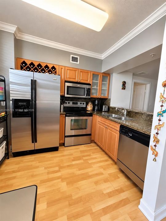 Kitchen featuring wood cabinetry with integrated wine storage, stainless steel appliances, stone countertops, double-basin sink, and wood-finish flooring