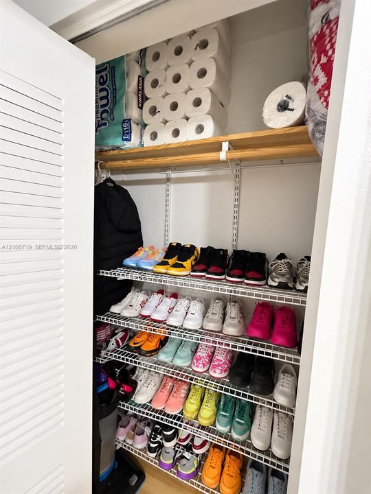 Storage closet featuring tiered wire shelving and a finished wood top shelf