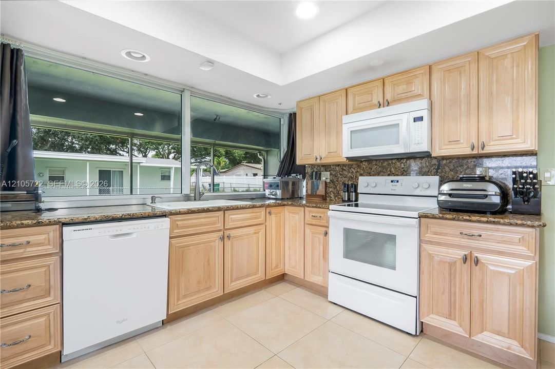 Kitchen featuring light-finish cabinetry, stone-texture countertops, large horizontal windows, tile flooring, and integrated white appliances