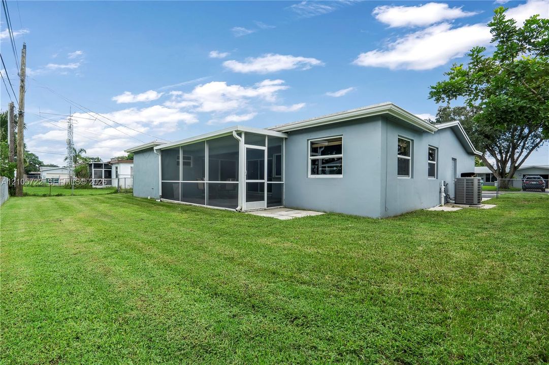 Rear exterior featuring a stucco facade, an attached screened-in patio, and an expansive lawn