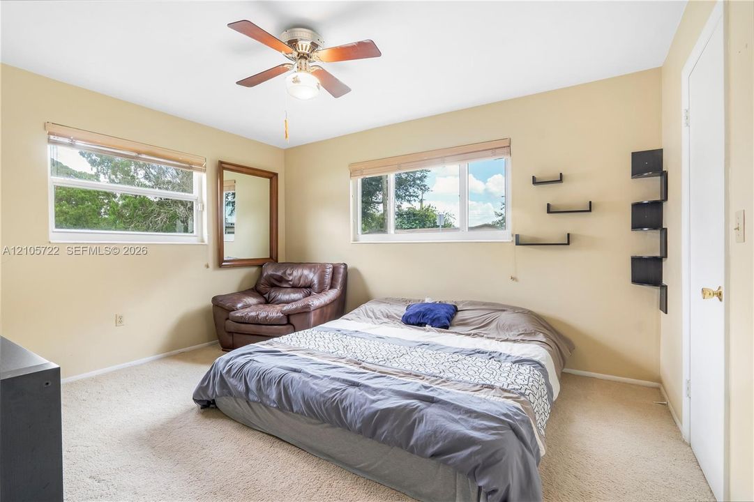 Dual windows providing natural light, central ceiling fan with integrated lighting, neutral wall color, and wall-mounted shelving