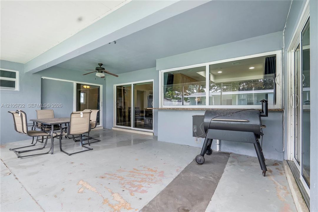 Covered patio featuring a concrete floor, built-in pass-through window with a stone-finish counter, and a ceiling-mounted fan
