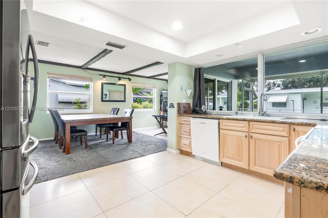 Kitchen featuring light-finish cabinetry, stone countertops, integrated dishwasher, tile flooring, and a recessed ceiling design with exposed wood beams