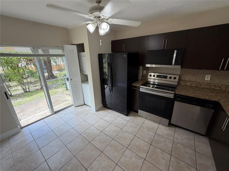 Kitchen featuring dark wood-finish cabinetry, stone-style countertops, stainless steel appliances, tile flooring, and a sliding glass door