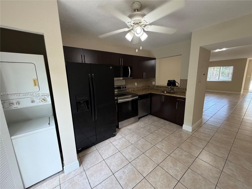 Kitchen featuring dark wood-finish cabinetry, stone-style countertops, stainless steel appliances, a ceiling-mounted light fixture, and tile flooring