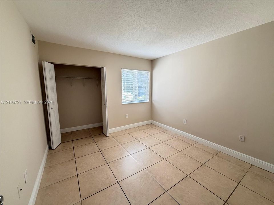 Neutral wall tones, large-format tile flooring, single window, and a built-in closet with louvered doors