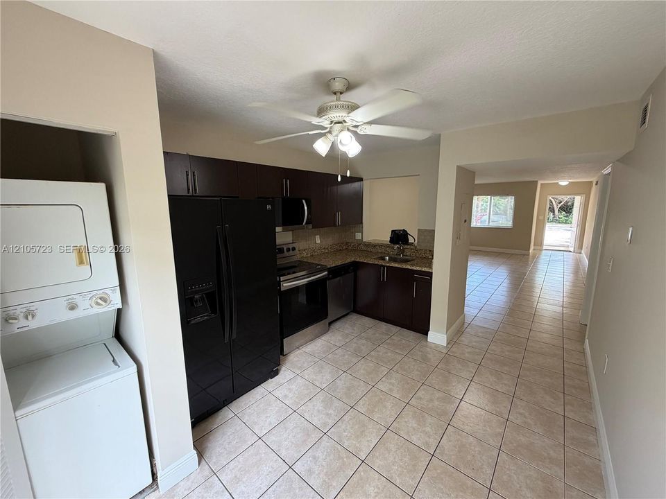 Kitchen featuring dark cabinetry, stone-finish countertops, stainless steel appliances, tile flooring, and ceiling fan with integrated lighting
