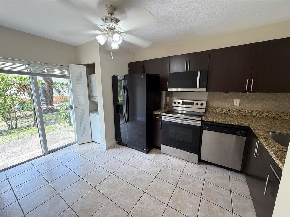 Kitchen featuring dark cabinetry, stone-finish countertops, stainless steel appliances, tile flooring, and glass sliding doors