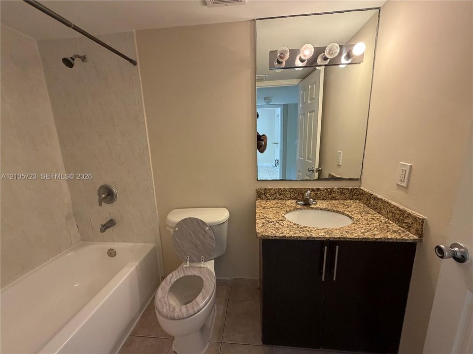 Bathroom featuring a vanity with stone-finish countertop, dark wood-tone cabinetry, a large wall-mounted mirror with multi-bulb light fixture, and a tile-surround shower and tub combination
