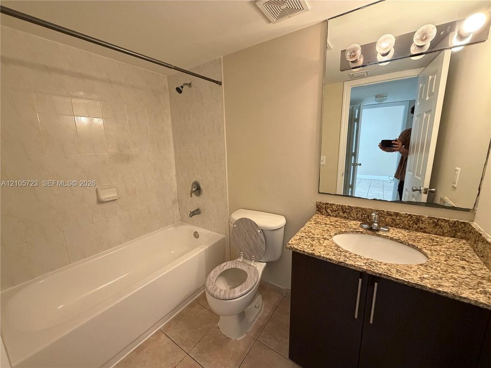 Bathroom featuring a stone-surface vanity with an integrated oval sink, dark cabinetry, large wall-mounted mirror, four-bulb light fixture, and a tile-surround bathtub
