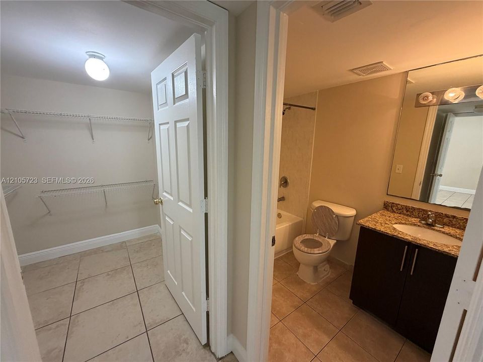 Bathroom featuring tile flooring, dark wood-finish cabinetry, stone-surface countertop with an integrated basin, and a bathtub with a shower surround