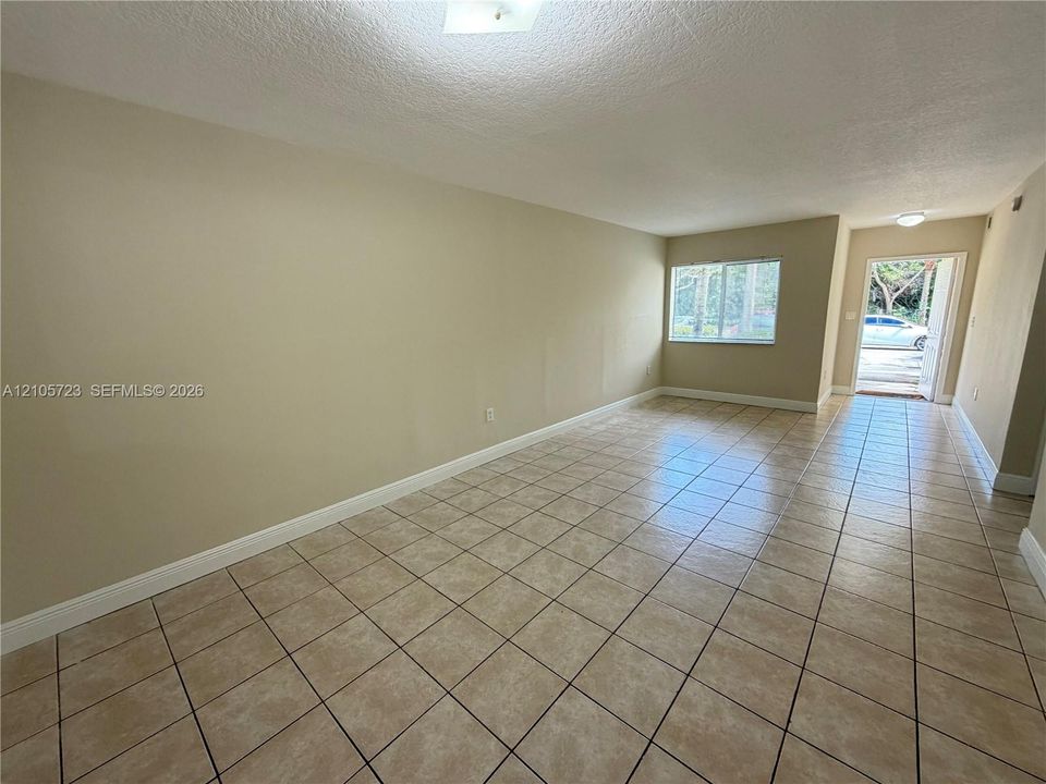 Neutral-toned interior featuring ceramic tile flooring, textured ceiling, and natural light via sliding window