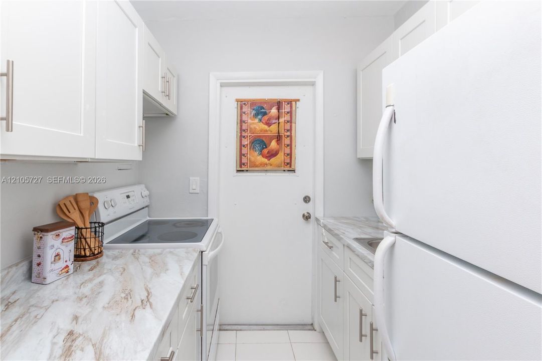 Kitchen featuring white shaker-style cabinetry, stone-finish laminate countertops, light-colored tile flooring, and white appliances