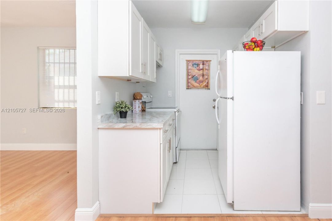 Kitchen featuring white cabinetry, stone-patterned laminate countertops, white floor tiling, and wood-finish flooring in the surrounding space