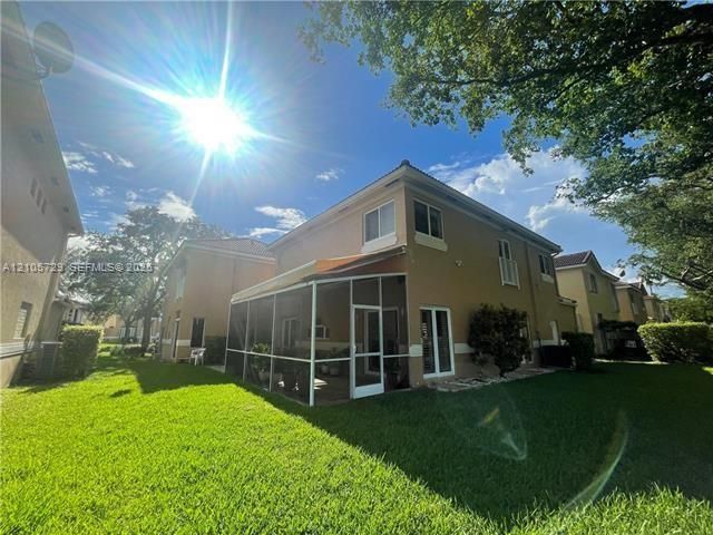 Two-story exterior featuring a stucco facade, a screened-in lanai, and a spacious grass yard with mature trees