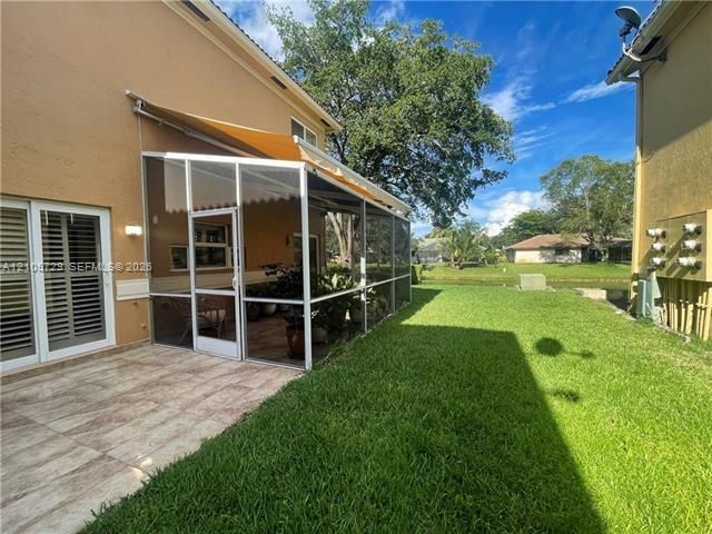 Screened-in patio with a retractable awning, stone-finish tile flooring, and a manicured lawn overlooking a canal