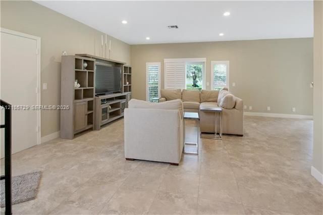 Living area featuring large-format tile flooring, recessed lighting, built-in wall shelving, and window shutters