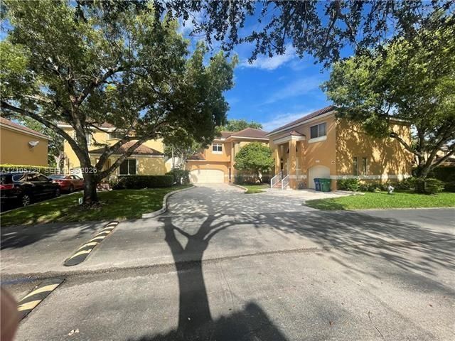 Stucco exterior with multi-level architectural design, paved driveway, attached multi-car garages, and mature shade trees