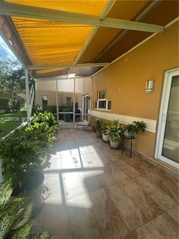 Covered screen-enclosed patio featuring oversized tile flooring, a retractable yellow awning, and exterior wall-mounted lighting