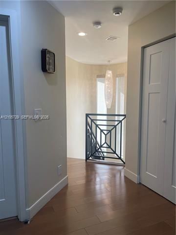 Hallway featuring wood-finish flooring, recessed lighting, a modern pendant light fixture, and black metal geometric railings