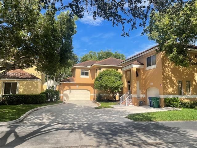 Stucco exterior featuring a multi-car garage, pitched tile roof, arched entryway with white railing, and a concrete driveway