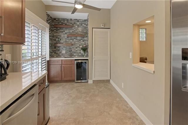 Wet bar featuring custom wood cabinetry, stone-tiled backsplash, built-in beverage refrigerator, floating wood shelving, and stone tile flooring