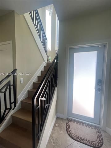 Foyer featuring a staircase with geometric black metal railing, wood-finish treads, stone-tile flooring, and an entry door with a frosted glass panel