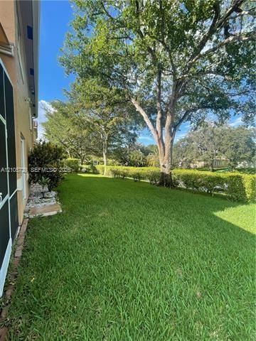 Spacious backyard featuring a manicured lawn, established landscaping, mature trees, and a stone-bordered planting bed